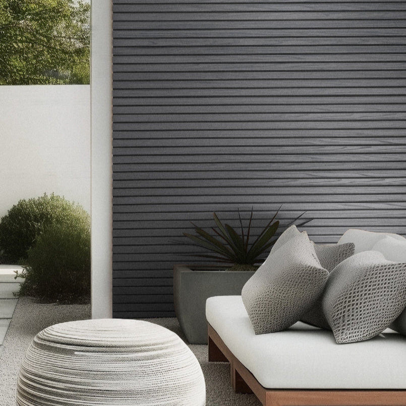 Outdoor seating area with a textured ottoman and cushioned bench against a gray panel wall.