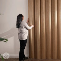 Person installing Flutto™ Oak Zigzag flexible wood panels in a modern interior setting.